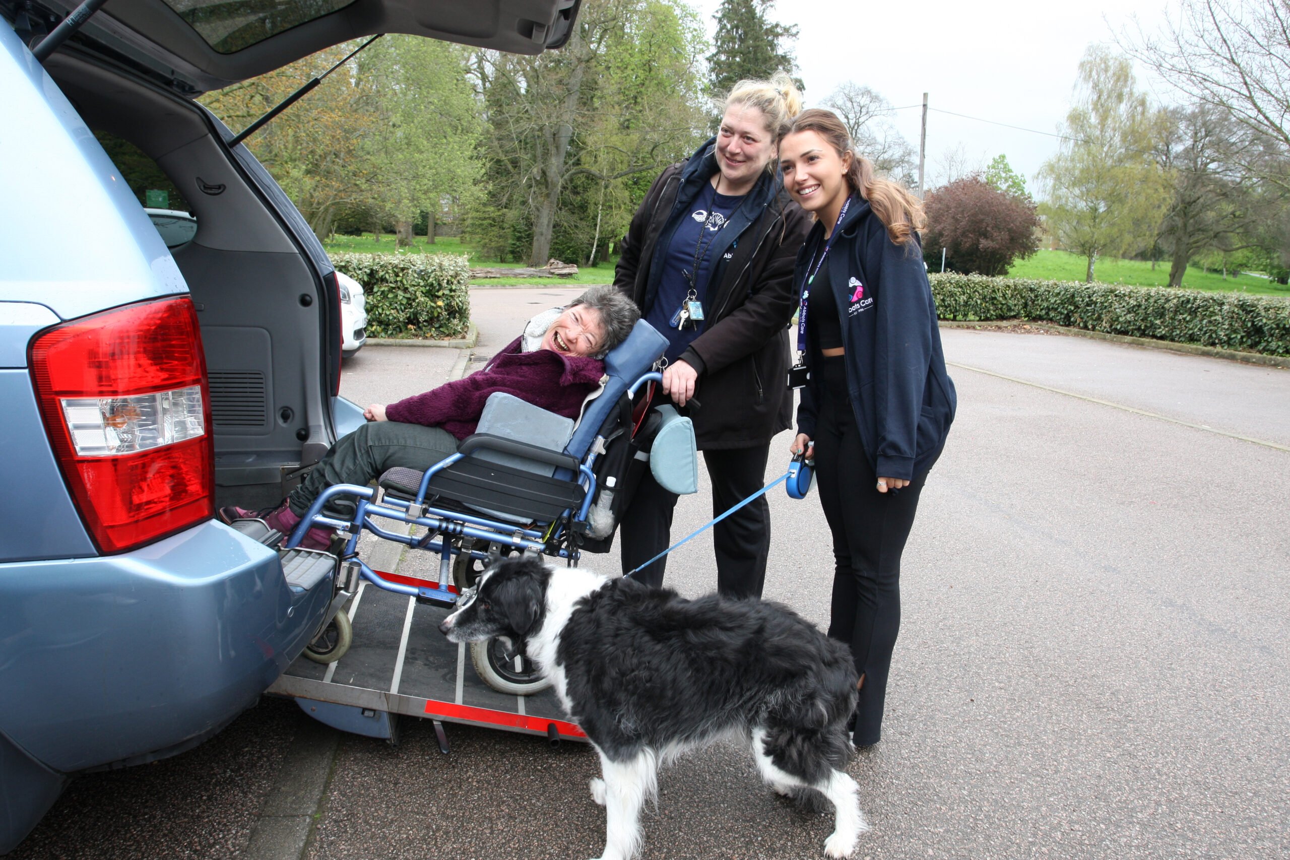 Care Workers aiding a client and her dog into a car