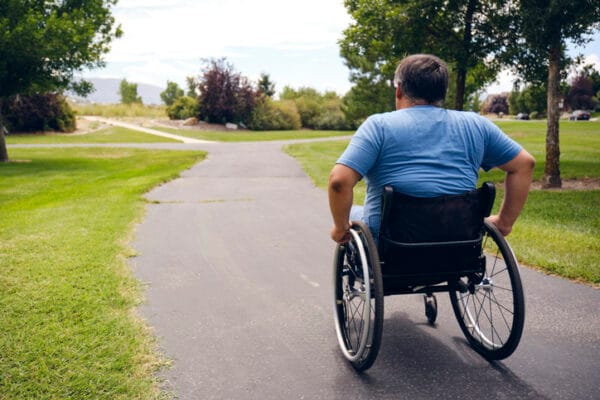 Man in wheelchair pushing himself a long a path in a park