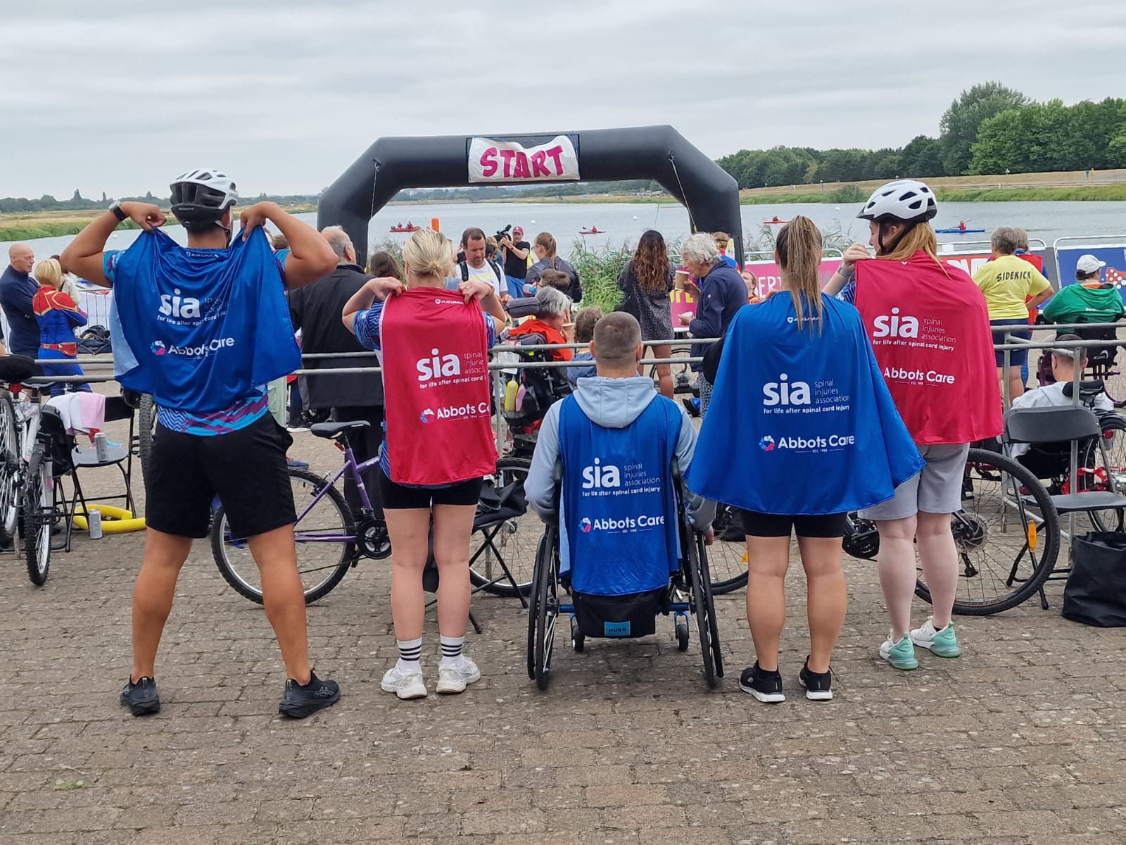 Abbots Care team members from behind wearing superhero capes featuring the Abbots Care and Spinal Injuries Association logos.