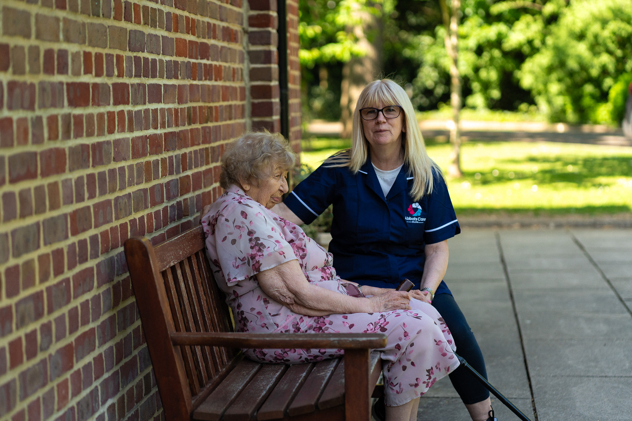 Tina, Abbots Care Worker, and June, abbots Care client sit on a bench