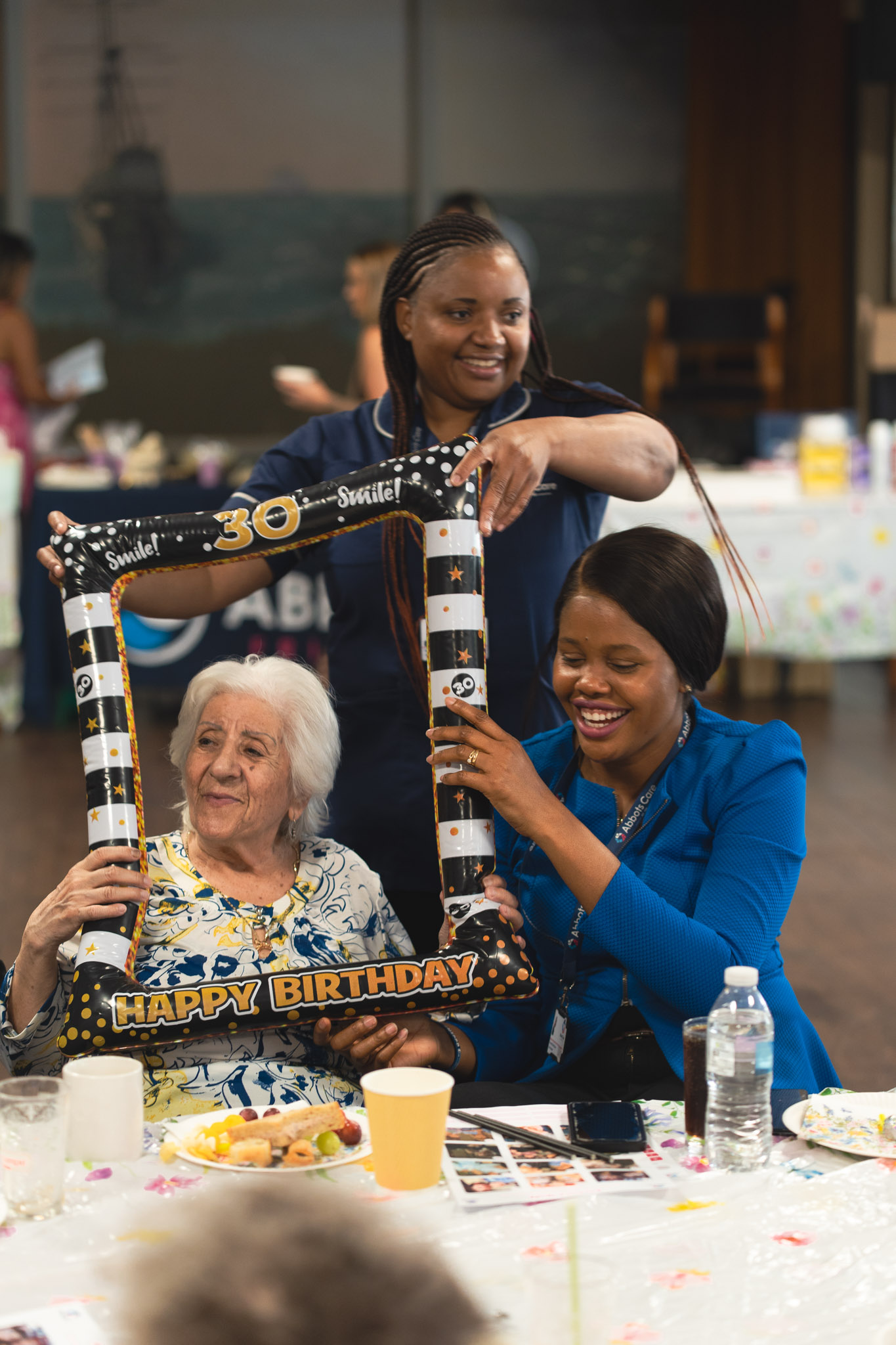 Two Abbots Care Workers smile as they pose with a client at an Abbots Care 30th Birthday tea party