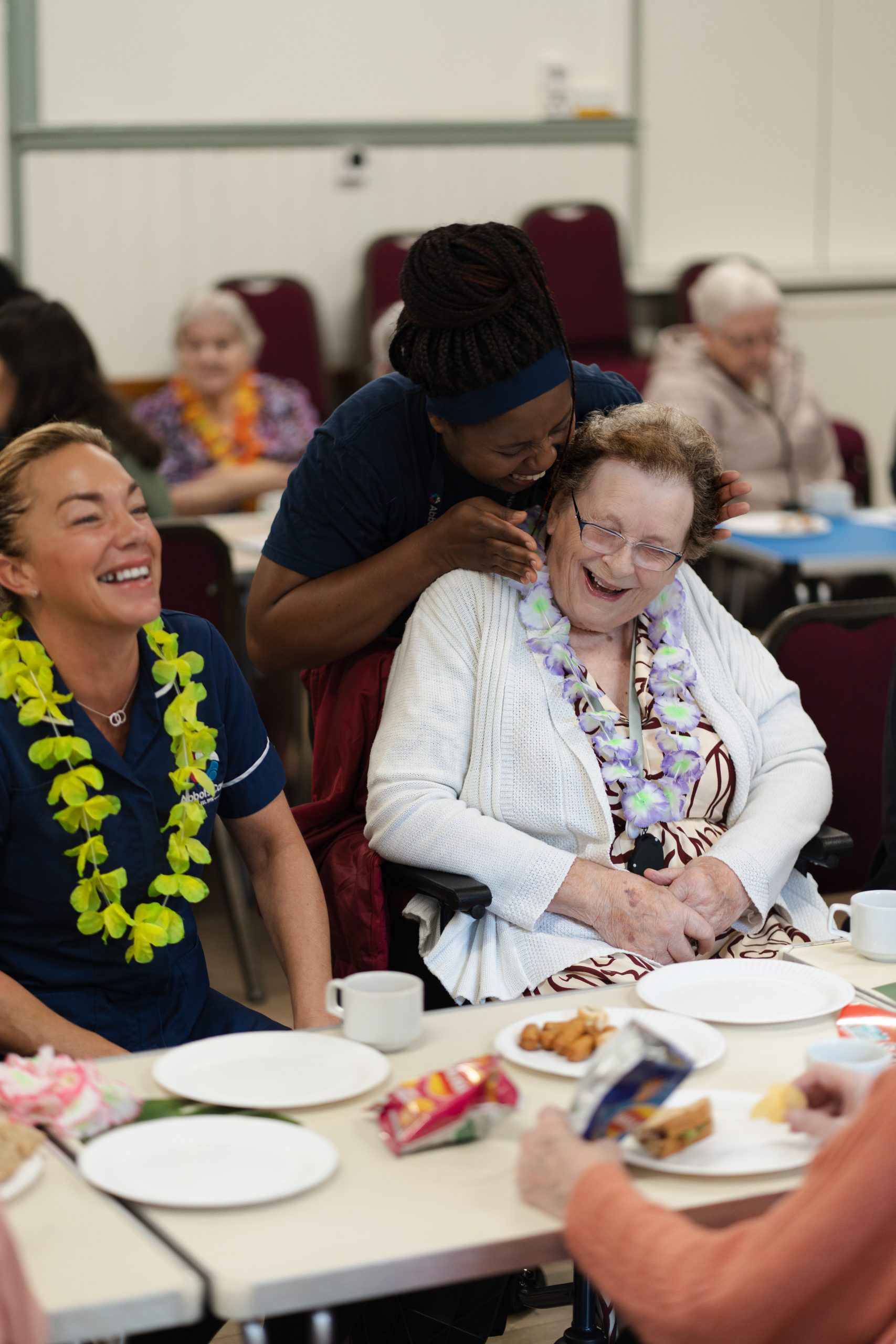 Two Abbots Care Workers laugh with a client at one of our client tea parties